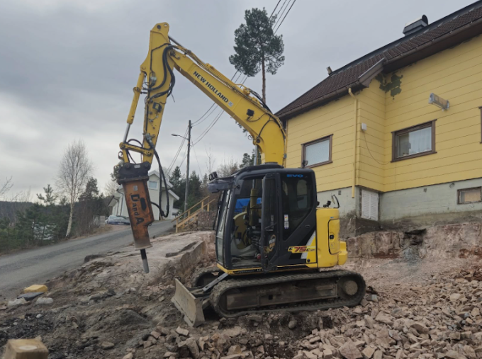 Gravemaskin foran gult hus